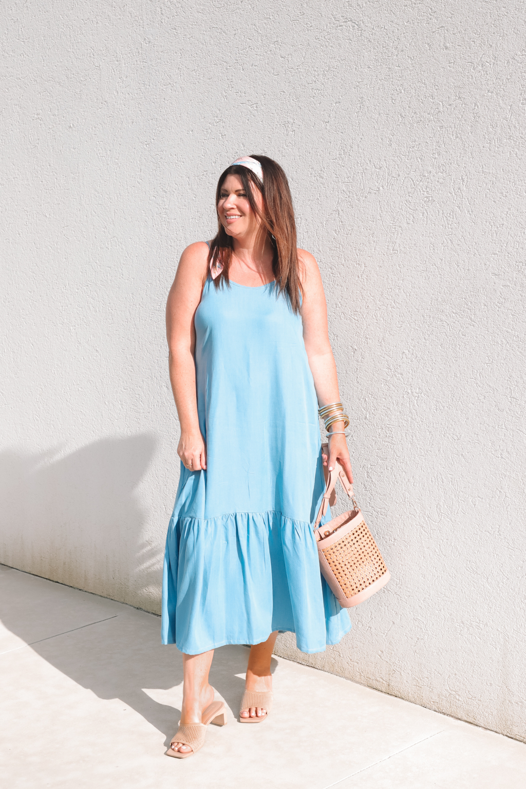 Woman in a light blue dress holding a woven bag against a white wall