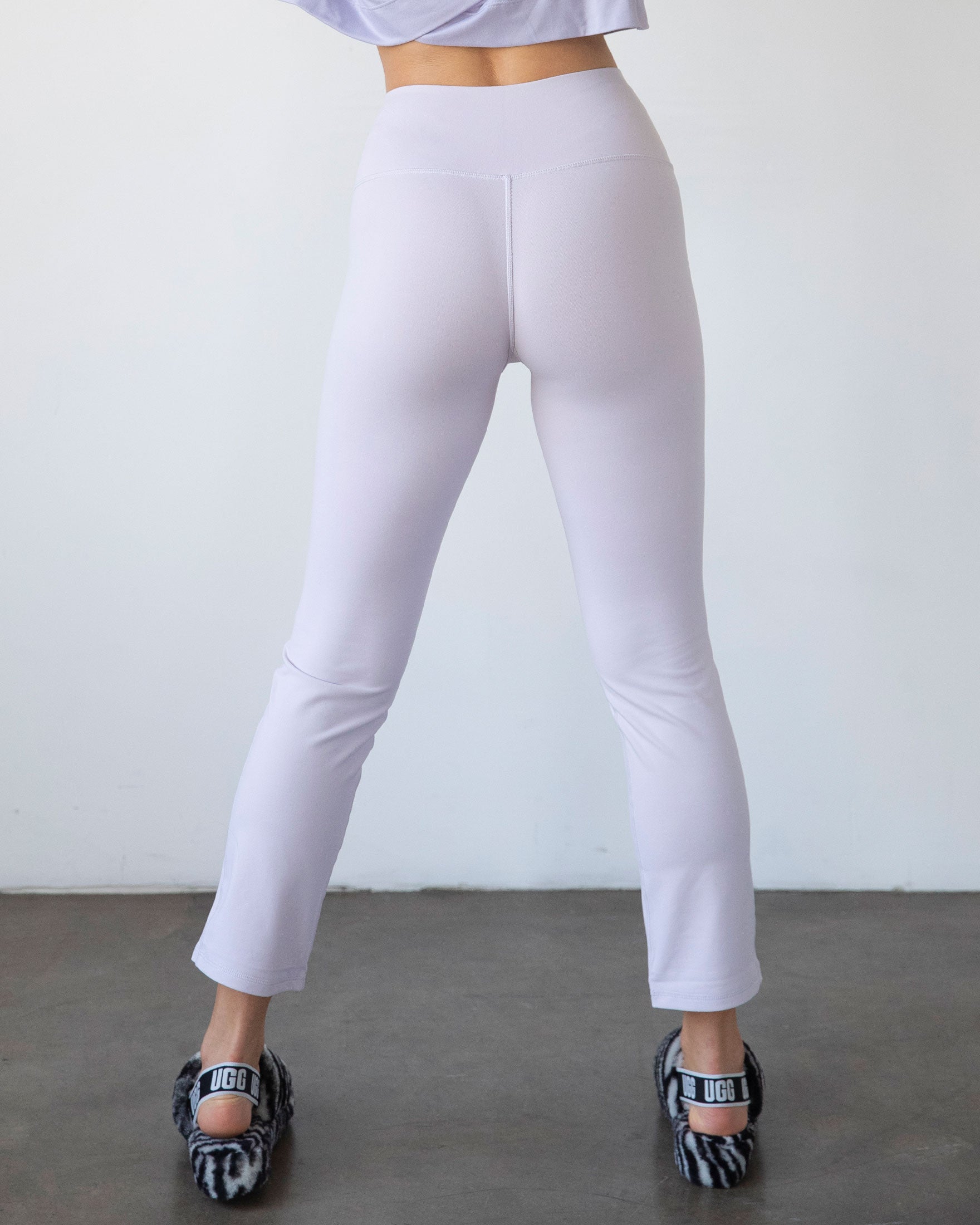 Person wearing light purple leggings and black and white shoes on a plain background