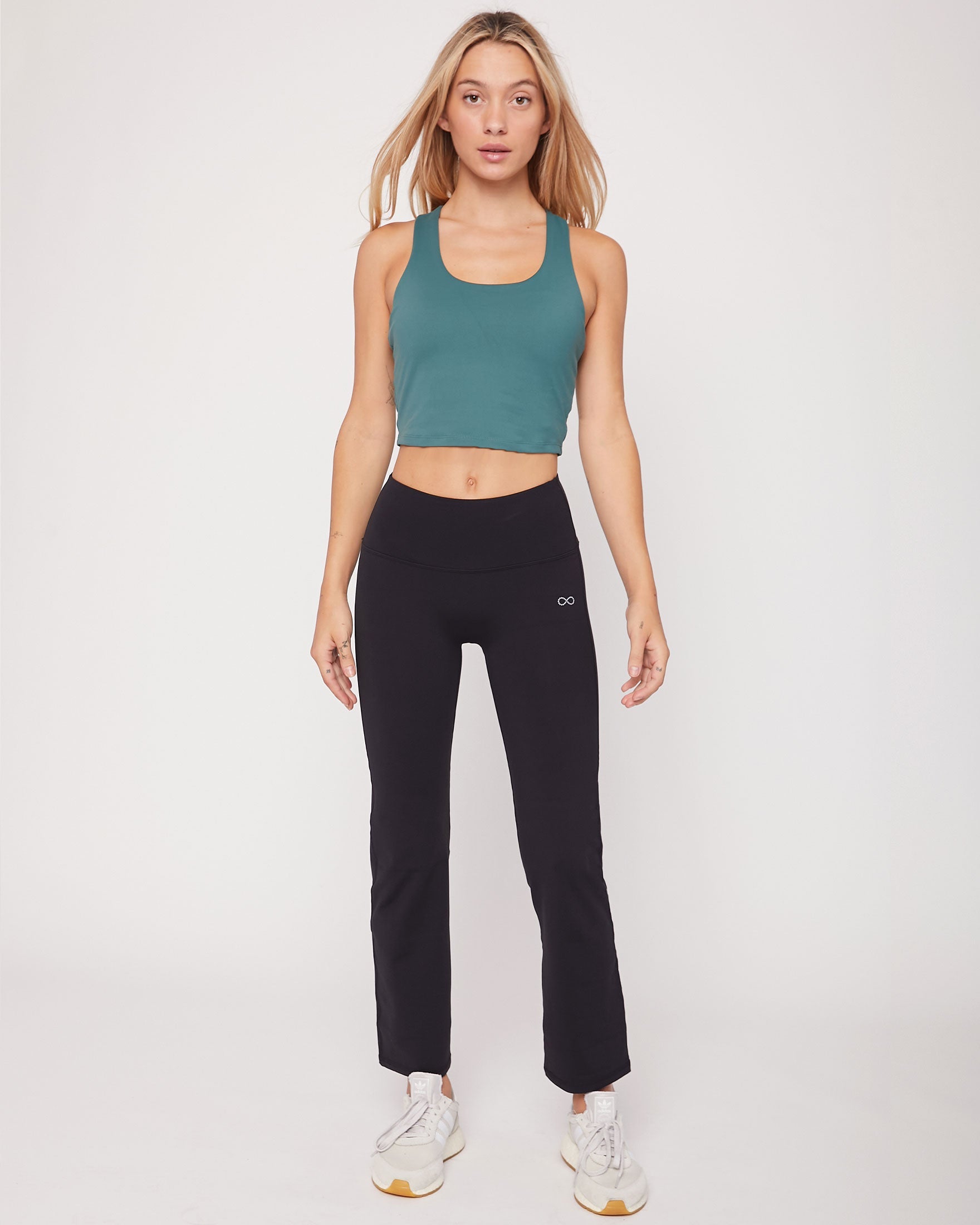 Woman wearing a green tank top and black leggings on a white background