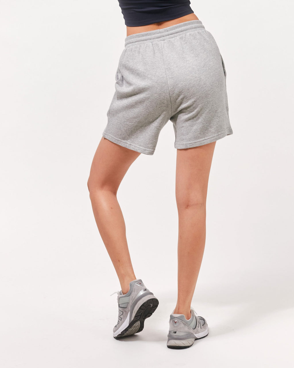 Person wearing gray shorts and gray sneakers on a white background